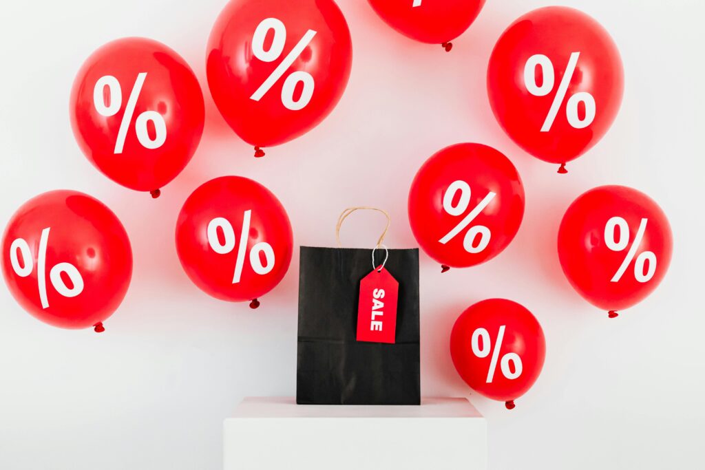Red balloons with percentages and a black sale bag on a white background.