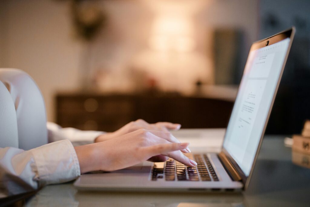 Close-up of hands typing on a laptop at home, showcasing a cozy work environment.