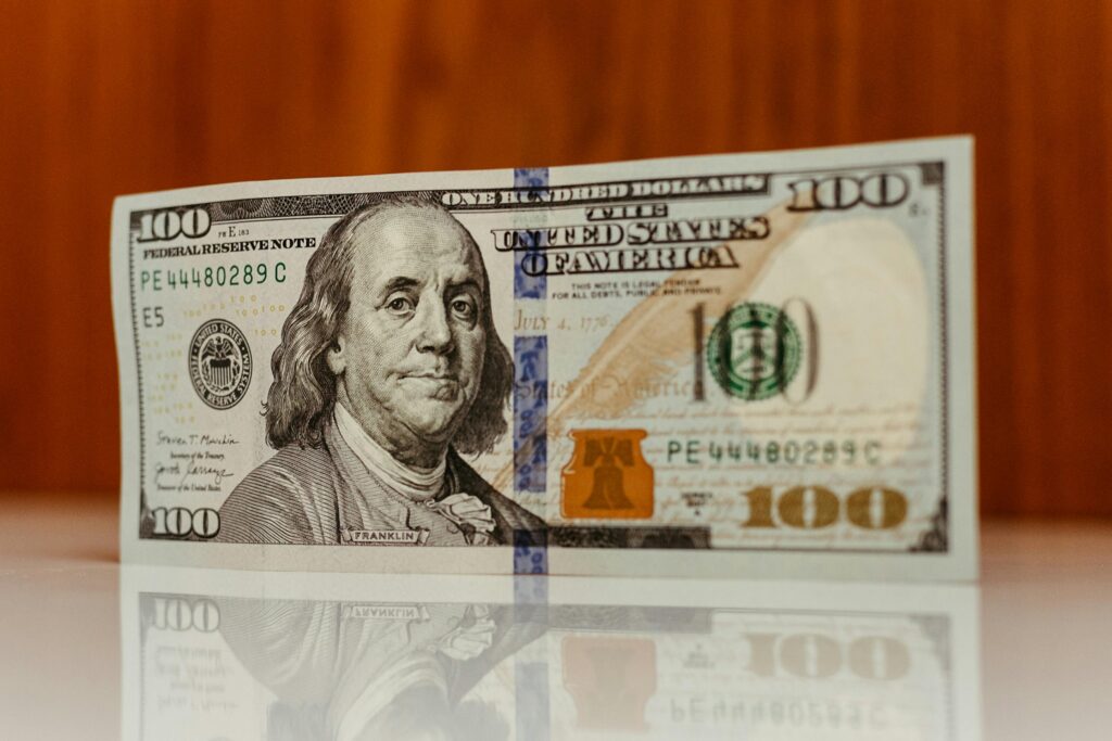 Crisp image of a $100 bill standing and reflecting on a smooth surface, highlighting details.