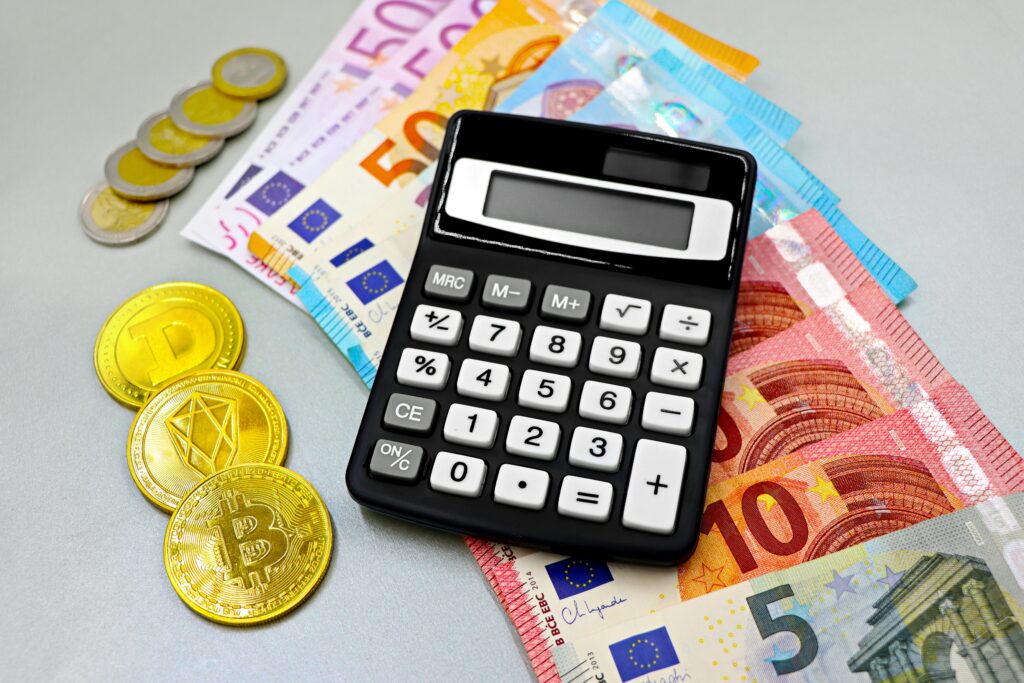 Calculator with euro banknotes and cryptocurrency coins like Bitcoin on a table.