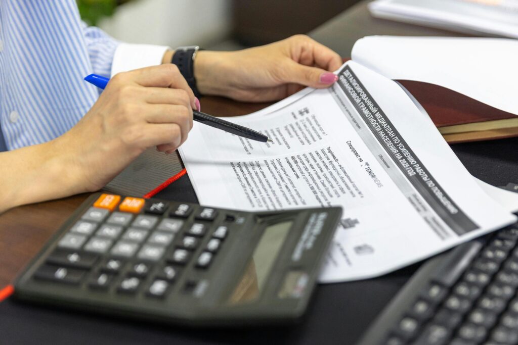 Close-up of a person analyzing financial documents using a calculator and pen.