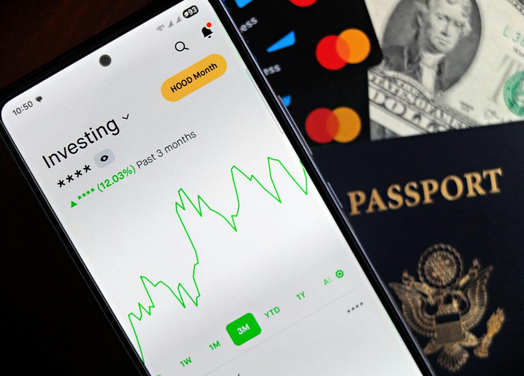 Smartphone showing stock market app with travel essentials: passport, money, and cards.