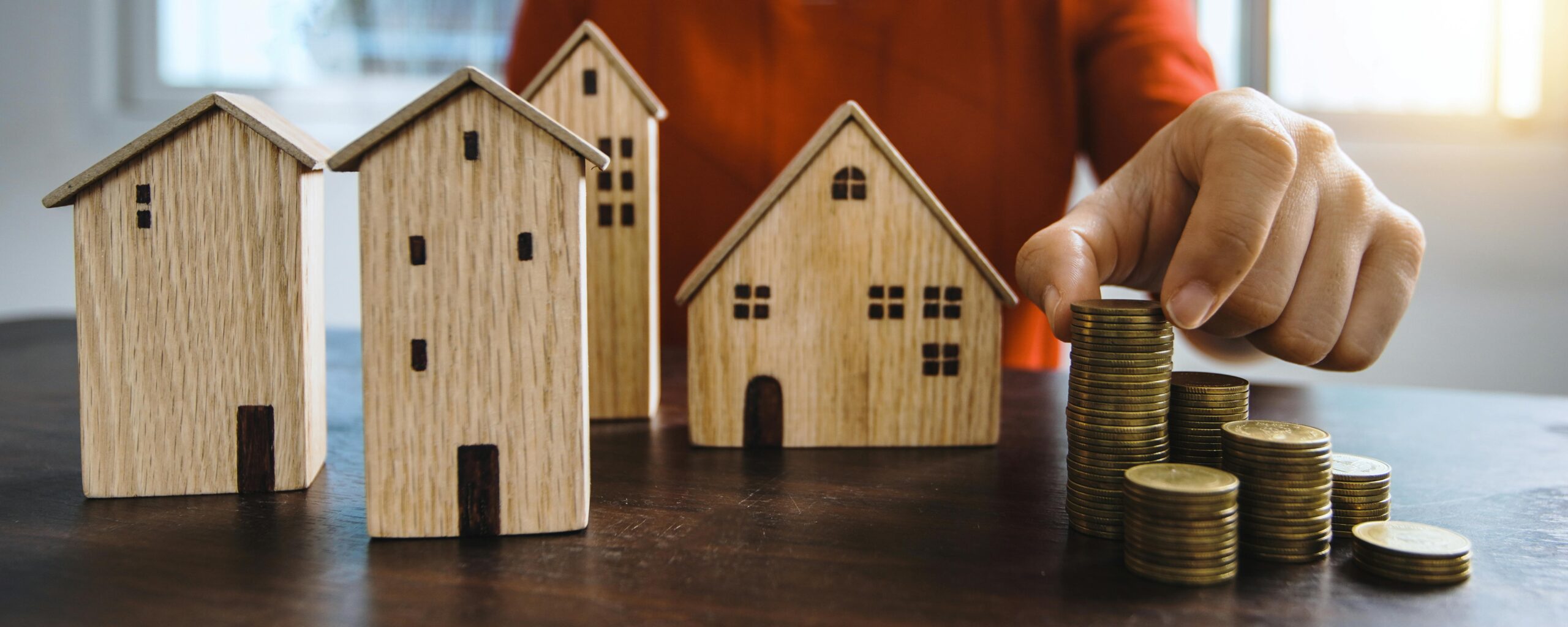 Real Estate Investing in 2026: REITs vs. rentals—what wins on cash flow? Planning investments with stacked coins and model houses on a table.