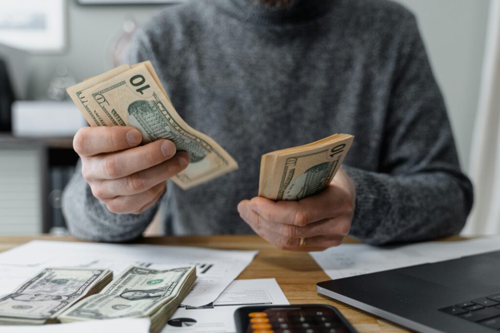 Close-up of person counting cash with a calculator and paperwork on a desk.