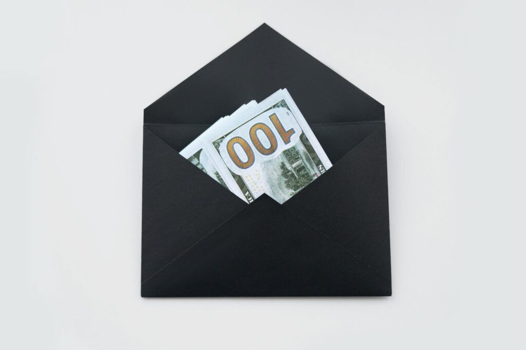 Hundred dollar bills partially visible in an open black envelope on a white background.