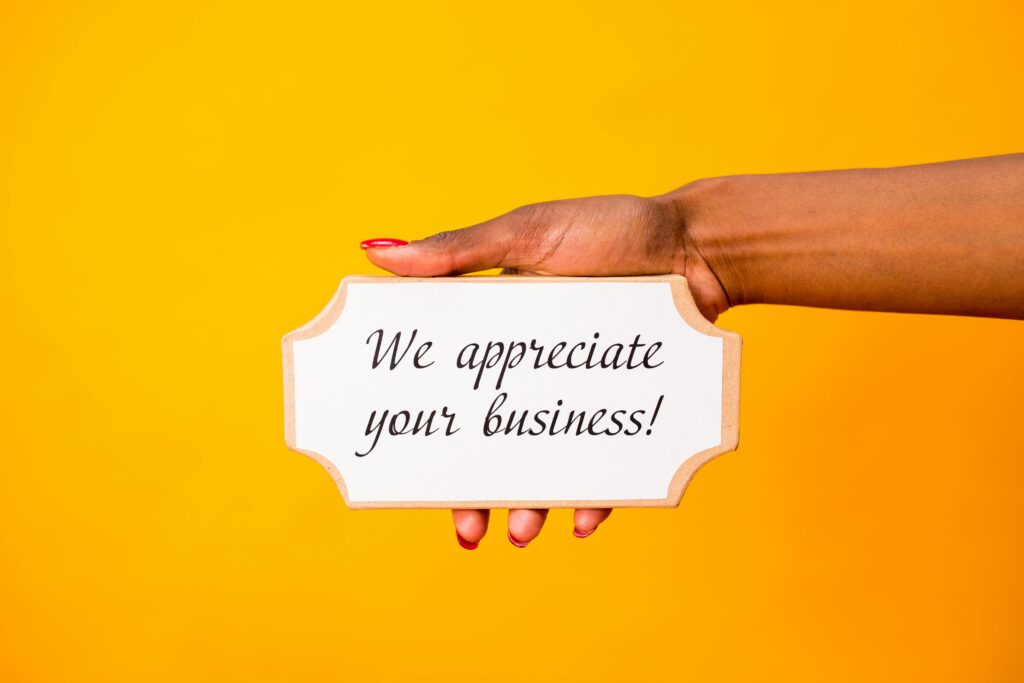 A hand holding a thank you sign with 'We appreciate your business!' on a vibrant yellow background.
