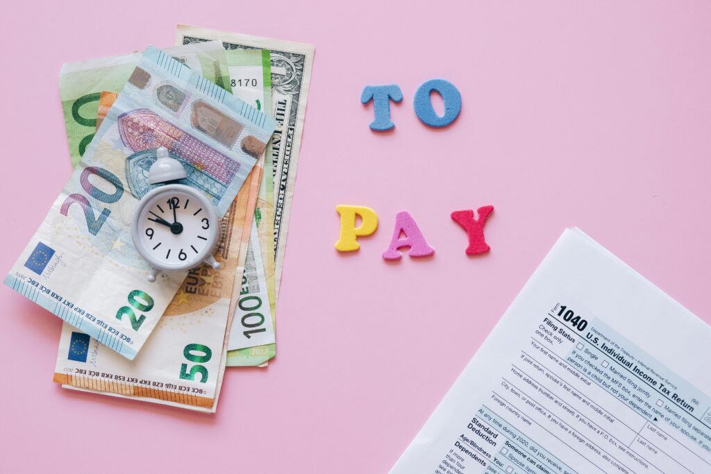 Flat lay of taxes, currency, and reminder to pay on pink background.
