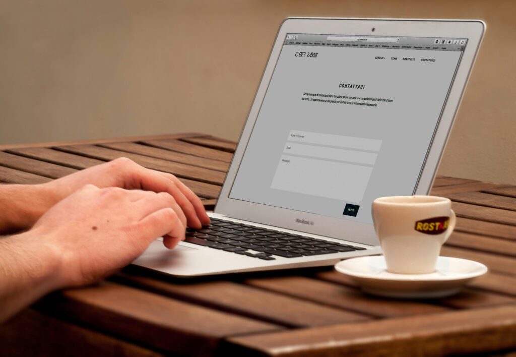 Close-up of hands typing on a laptop next to a cup of coffee on a wooden desk.