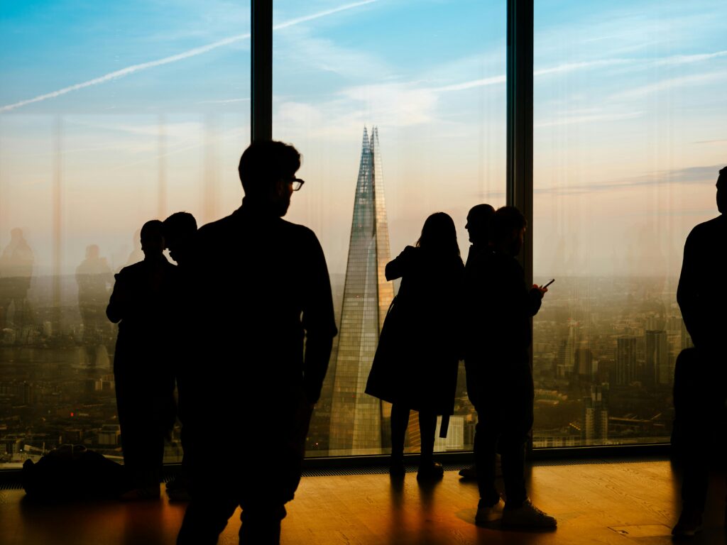 Silhouettes of people by a window overlooking London's iconic skyline during sunset, featuring The Shard prominently.