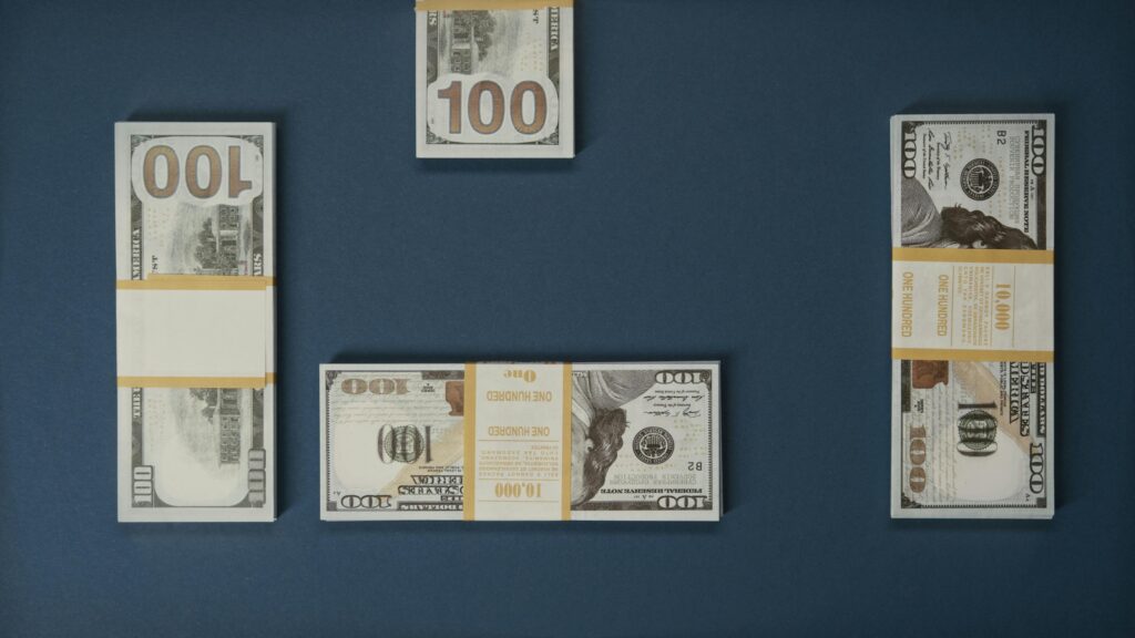 Flat lay of multiple stacks of 100 dollar bills on a blue background, symbolizing wealth and finance.