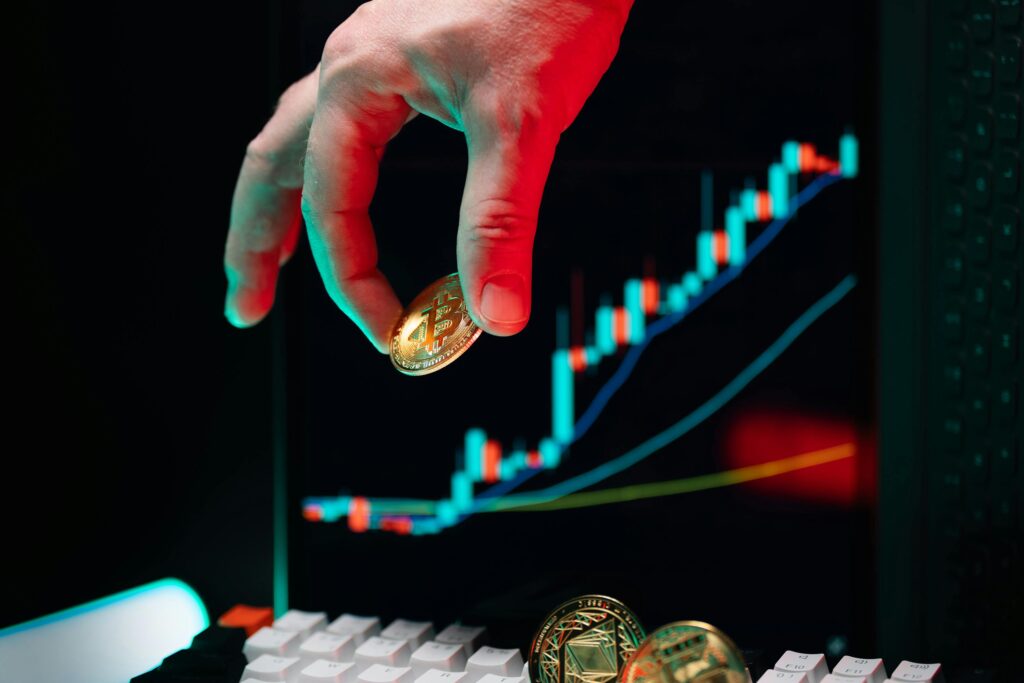Hand holding Bitcoin with an upward cryptocurrency market chart on screen displaying growth.