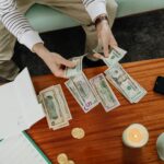A person sitting and counting various US dollar bills at a table indoors.