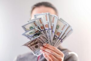A close-up of a person holding a fan of US dollar bills, signifying wealth and financial success.