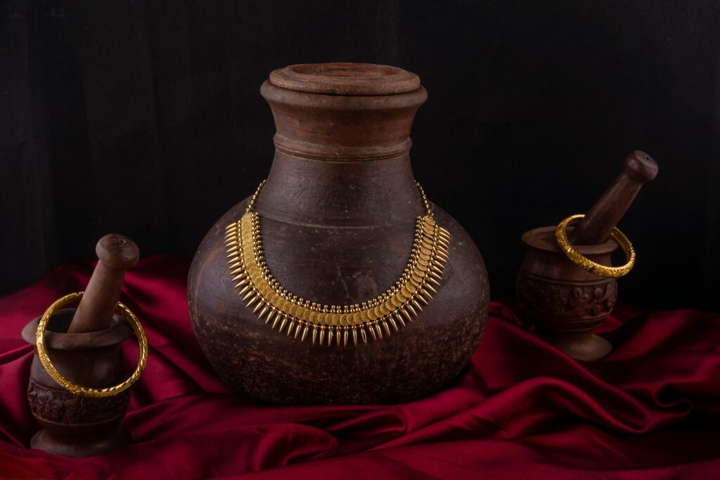 Elegant still life of traditional Indian necklace and bangles on vintage pottery with red fabric backdrop.