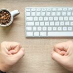Top view of a desk with coffee beans cup, keyboard, plant, and fists. Ideal for business and technology themes.