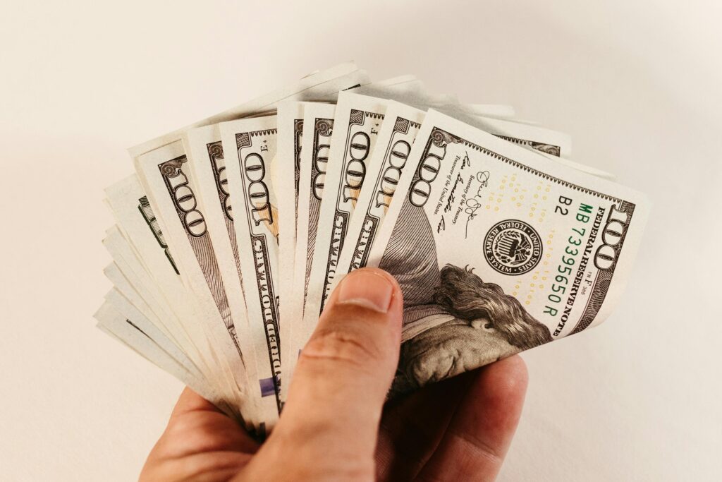 Close-up of a hand holding multiple US dollar bills against a white background.