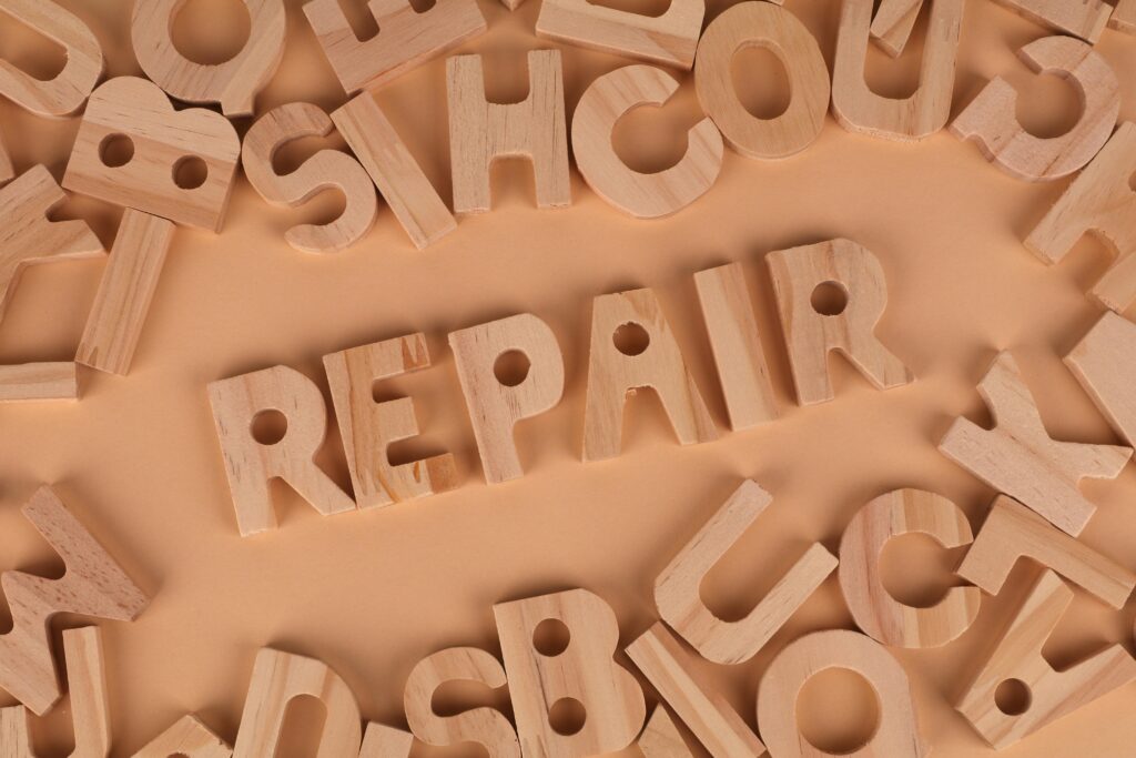 Top view of wooden letters arranged to spell 'REPAIR' on a beige background, perfect for DIY themes.