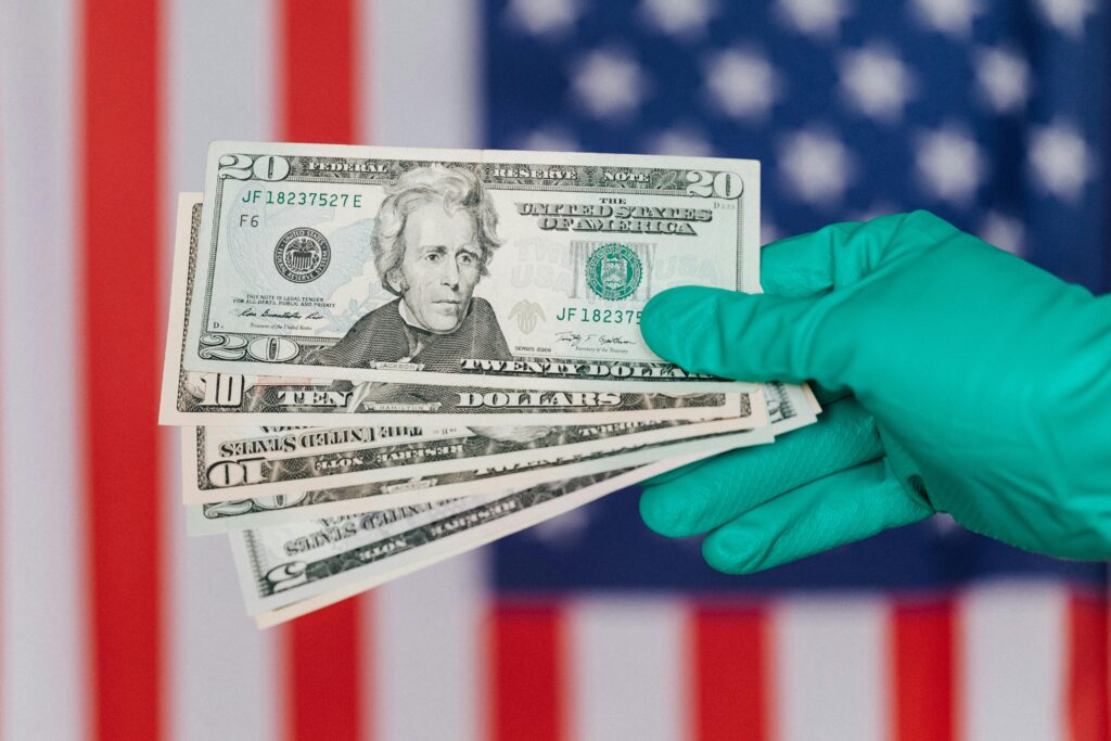 Closeup anonymous person in disposable gloves showing dollars near red and blue flag of United States