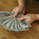 Close-up of hands holding several 100 US dollar bills on a wooden surface.