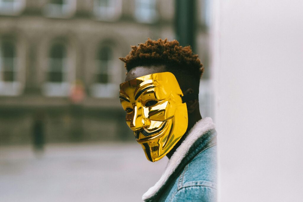 Unrecognizable African American activist wearing golden Anonymous mask as sign of disagreement with current state policy against building placed in city district in daytime