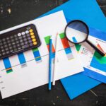 Top view of financial charts with a smartphone calculator, magnifying glass, and pencils on a desk.